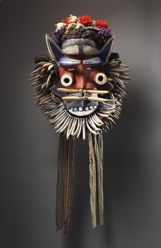 Through bold color and aggressive imagery, predatory animal references, horns, and strange tubular eyes this mask is a visually intimidating presence that harnesses the power of spirits from the wilderness as instruments of proprietary control in the realm of the town or village. Their visual affect was only heightened during performance. This Wé mask presents a bewildering accumulation of animal references: a fringe of aluminum-silver pseudo-leopard teeth, wild boar tusks, and pointed ears. With its bold color and bullet casings, this prototypical nature spirit mask is wild and menacing, making it a powerful judge during legal disputes and a great motivator of men preparing for battle.
