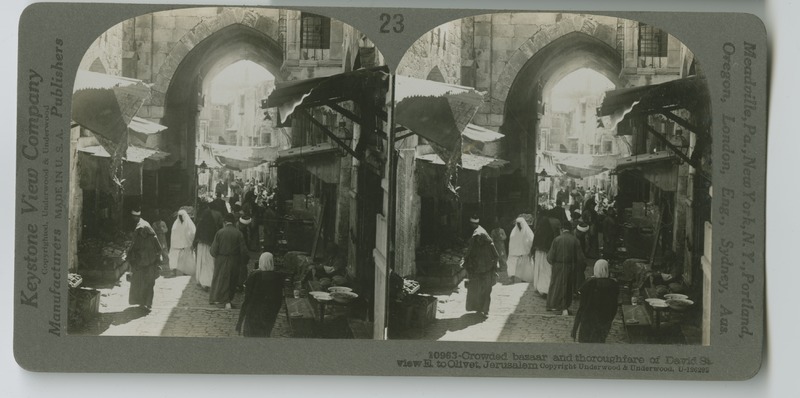 A view of David Street in Jerusalem, facing East towards the Mount of Olives. Crowds line the street where shops sell their wares.